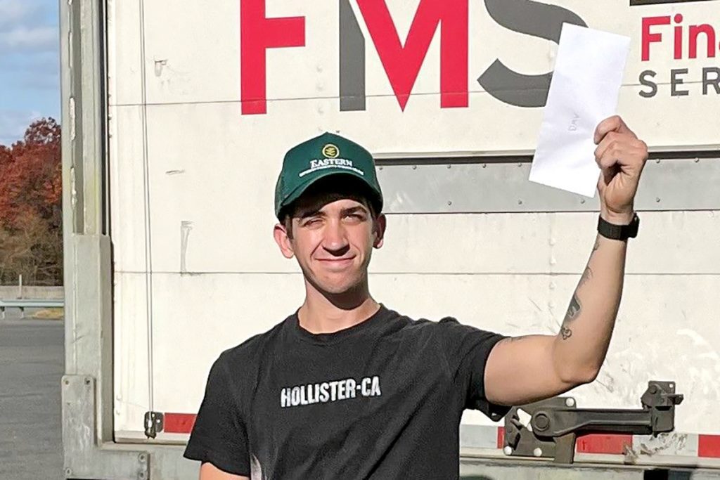 A man standing behind a large trailer holding up a piece of paper.