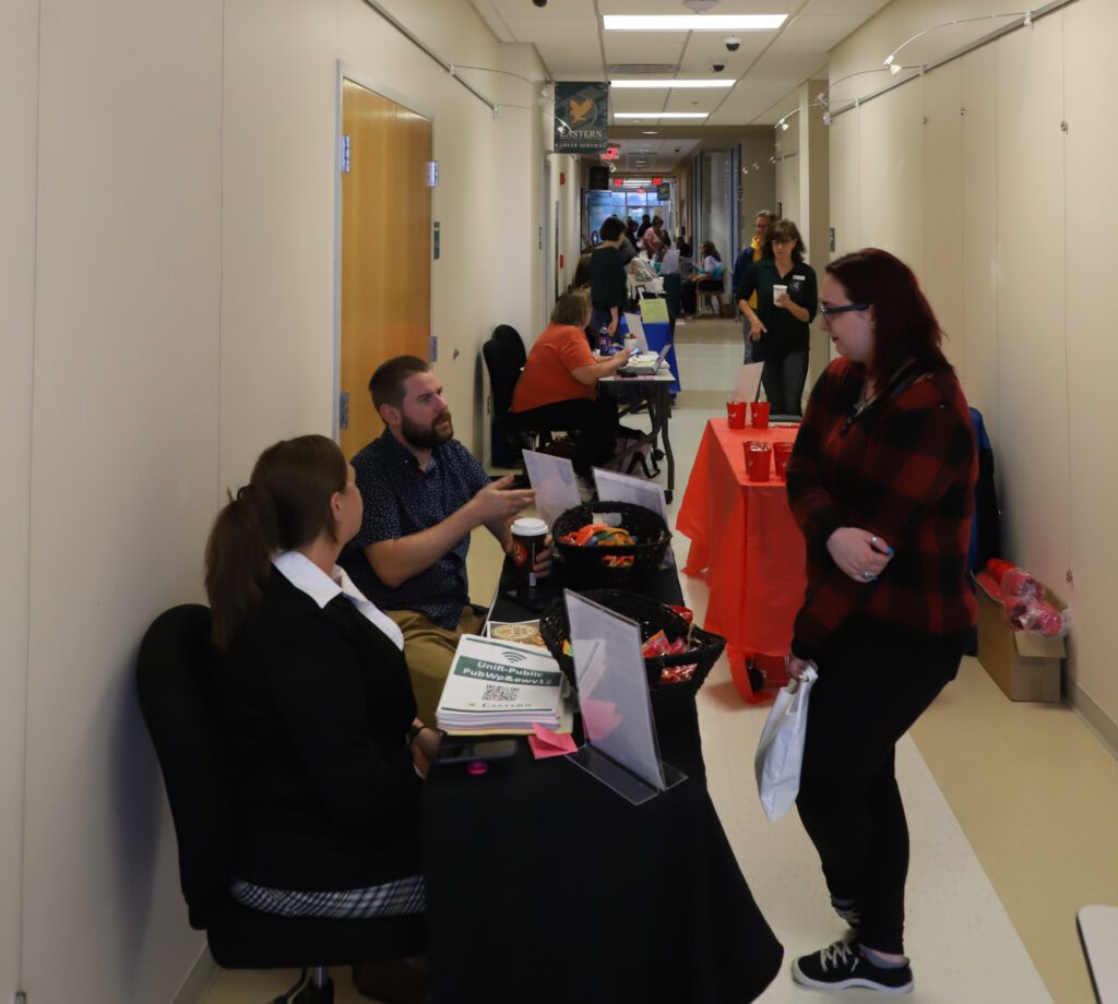 Group of people in a long hallway with tables set up along the hall.