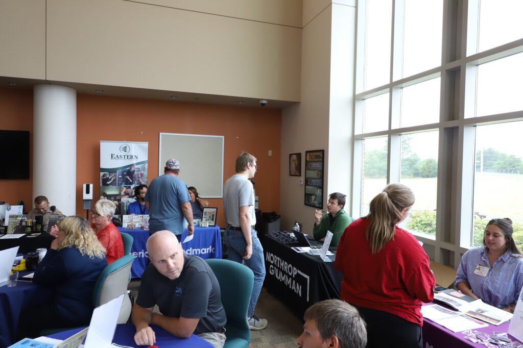 Photo of a man standing and speaking with someone sitting at a table.