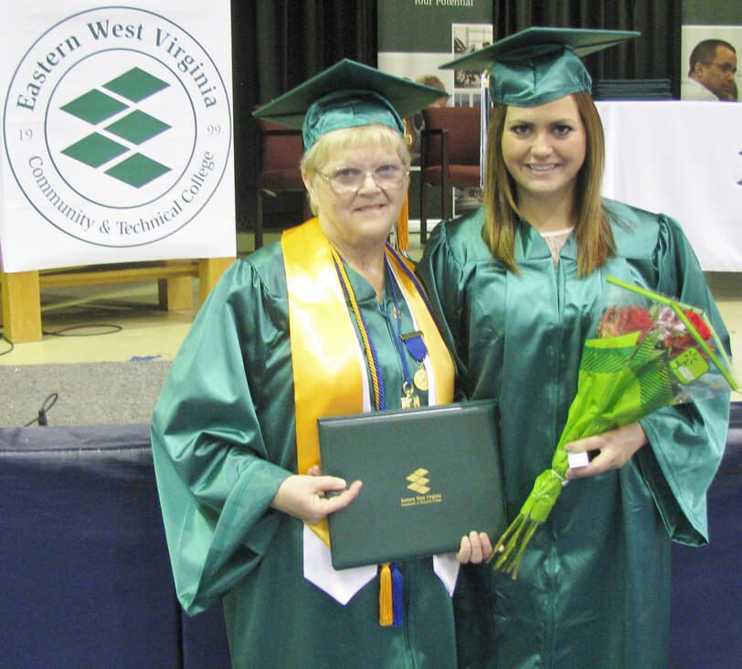 Photo of two women in their cap and gowns holding a diploma and bouquet of roses.