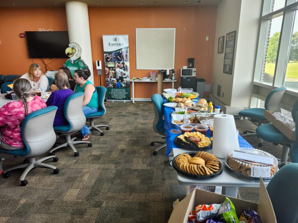 Photo of people sitting down and food laid out on the table to the right.