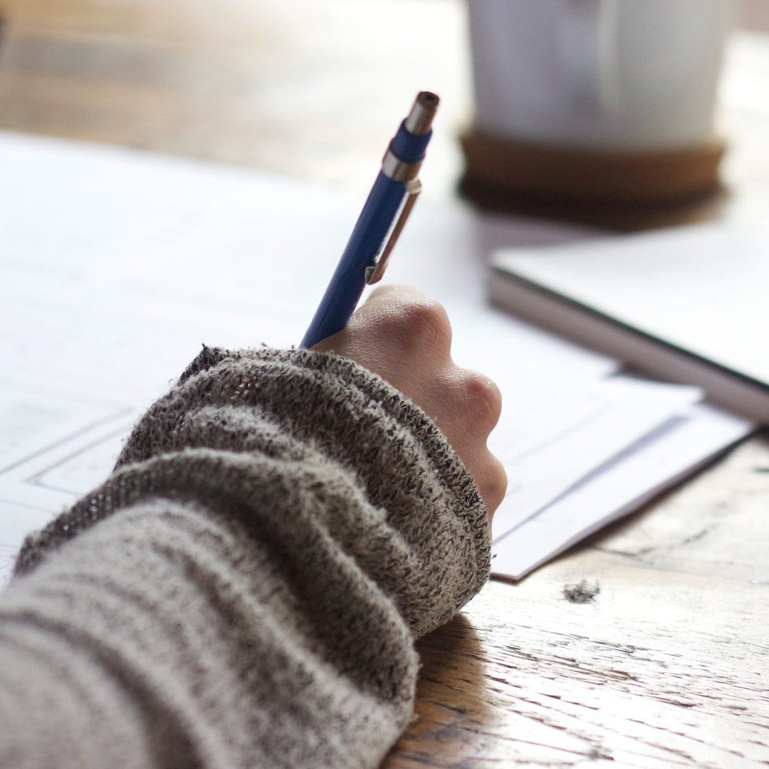 Photo of person holding a pen and writing on paper.