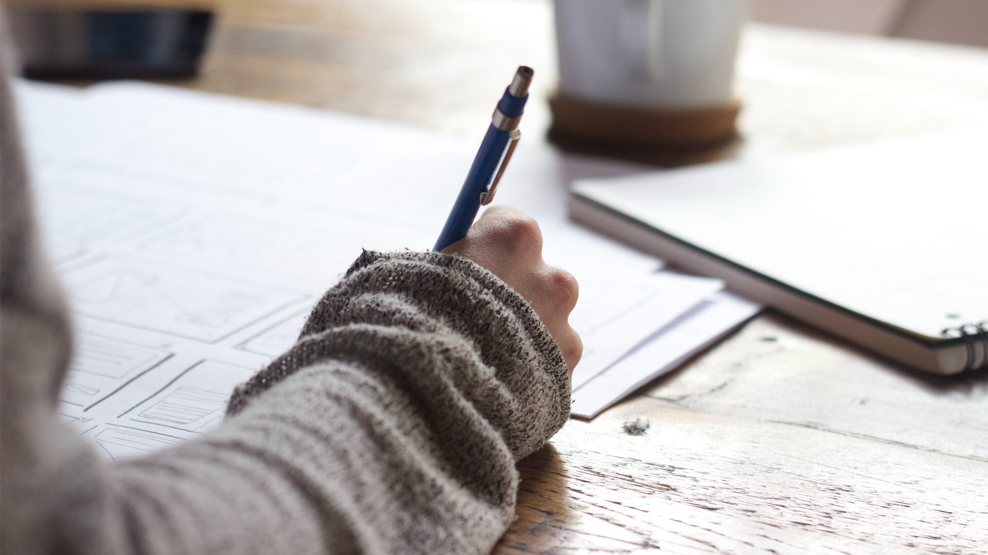 Photo of person holding a pen and writing on paper.
