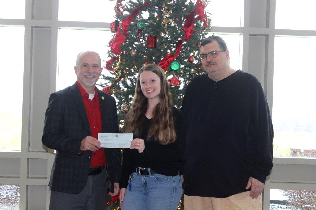 Two men presenting a woman with a scholarship check.