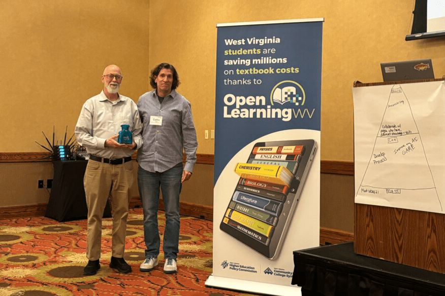 Photo of two men standing next to a banner on 'Open Learning." A podium is to the right of the banner.